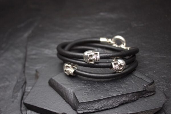 Black leather bracelets with silver skull beads on a dark slate surface.