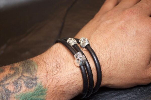 Close-up of a wrist wearing a black leather bracelet with silver heart charms.