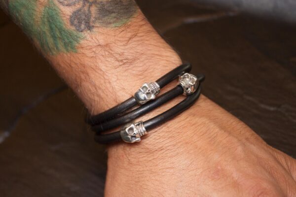Black leather bracelet with silver skull charms on wrist.