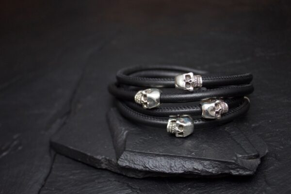 Black leather bracelets with silver skull charms on a dark surface.
