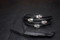 Black leather bracelets with silver skull charms on a dark surface.