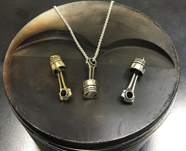 Pendant necklace crafted from a piston and connecting rod on a dark surface.