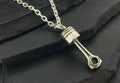 A silver piston-shaped pendant on a chain necklace.