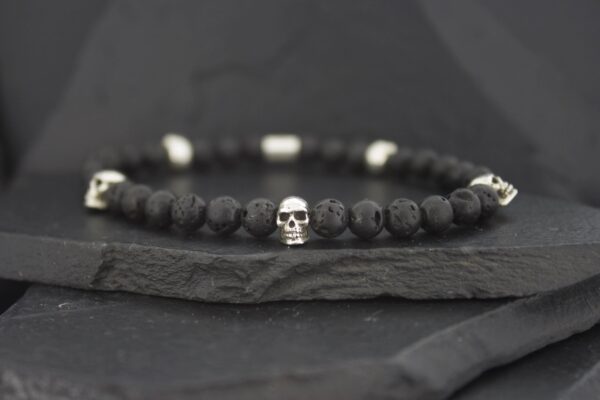 Black beaded bracelet with a silver skull charm on a dark stone slab.