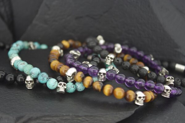 Beaded bracelets with skull charms in various colors on a dark surface.