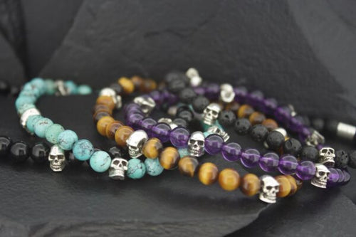 Beaded bracelets with skull charms in various colors on a dark surface.