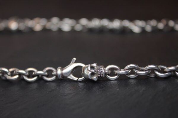 Close-up of a silver chain bracelet with a lobster clasp on a dark surface.