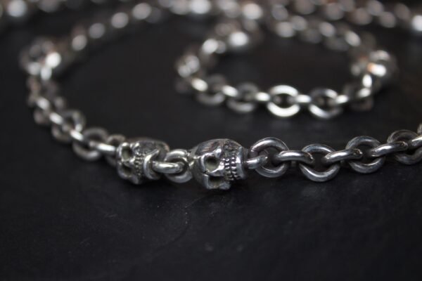 Close-up of a silver chain with skull-shaped links on a dark surface.