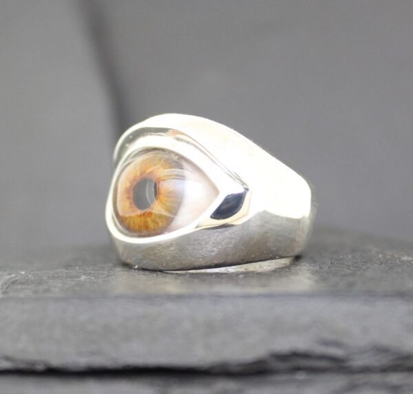 A silver ring featuring a detailed amber-colored eye design.