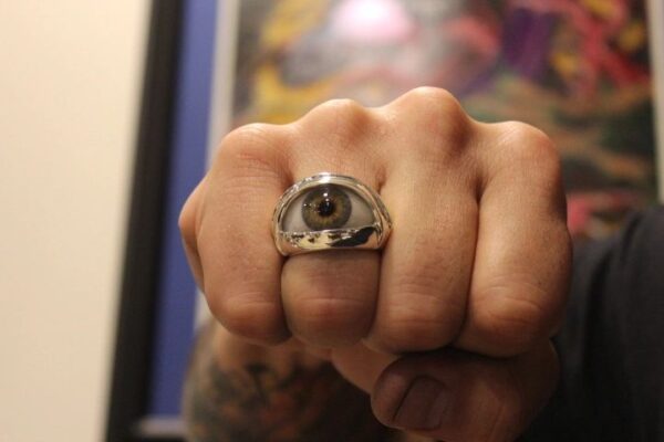 A hand wearing a ring with a realistic eye design on the knuckle.