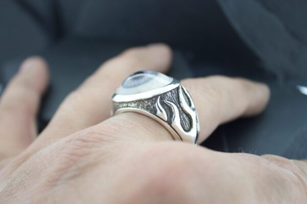Close-up of a silver ring with intricate black patterns on a finger.