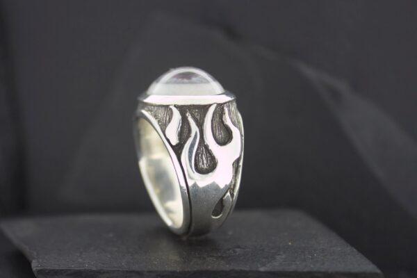 Silver ring with flame designs and a clear dome-shaped stone.