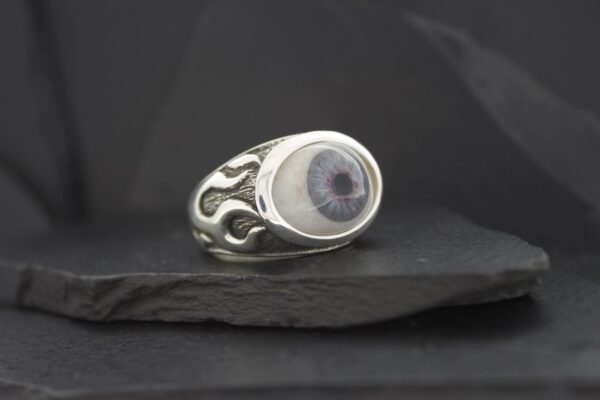 Silver ring featuring a detailed eye design on a dark background.