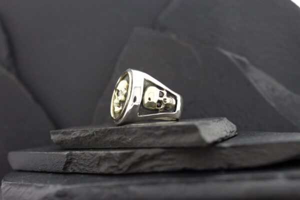 A silver ring with skull and crossbones design on a dark surface.