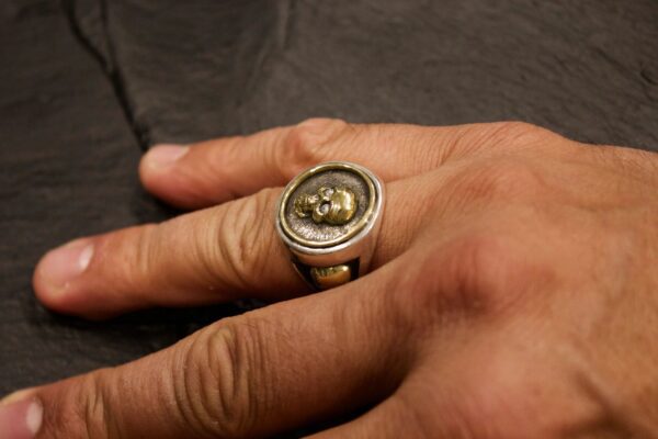 A hand wearing a thick silver ring with a large round gemstone.