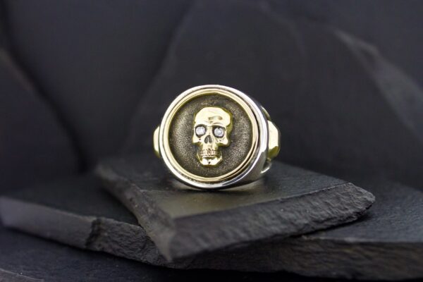 Silver ring with a detailed skull design on a dark stone background.