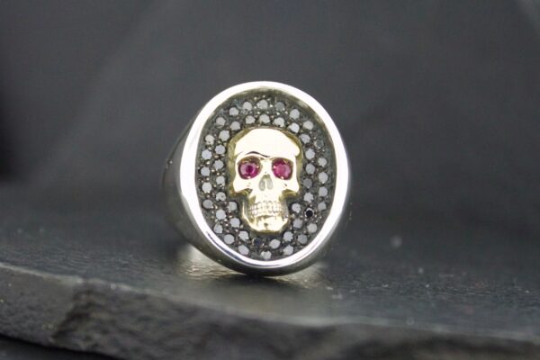 Silver ring with a skull featuring red eyes and intricate detailing.