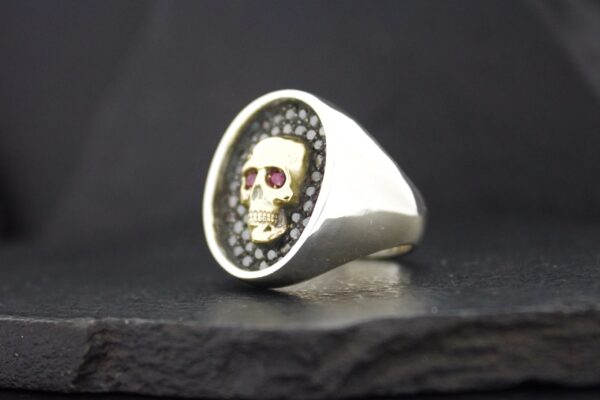 Silver ring with a skull design on a dark background.