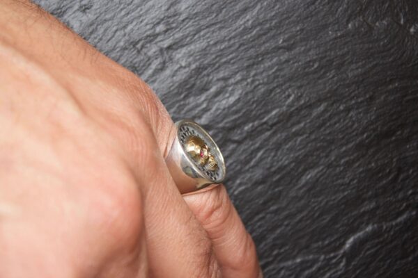 Close-up of a hand wearing a silver ring with a stone on a dark textured surface.