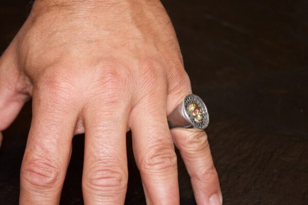 Hand wearing a silver ring with a clock face design.