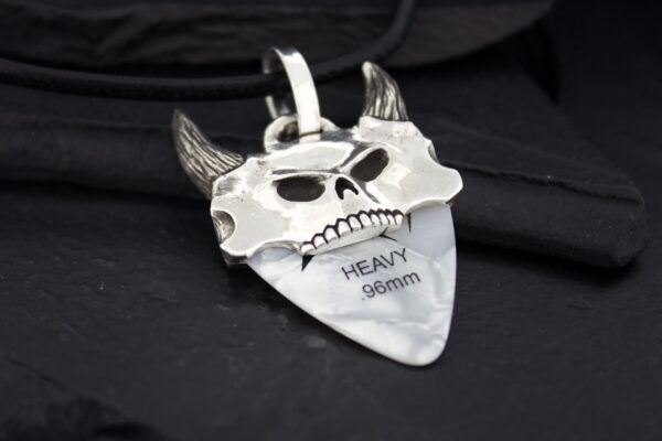 A silver pendant shaped like a devil's face with horns and engraved text.