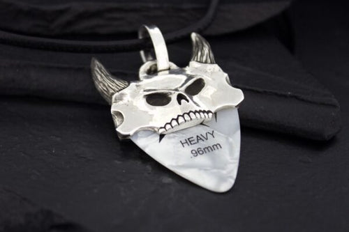 A silver pendant shaped like a devil's face with horns and engraved text.