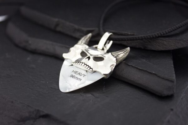 A silver pendant shaped like a horned skull with engraved text.
