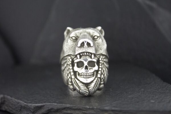 A silver ring featuring a bear and a skull design.