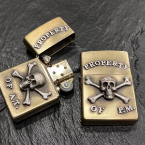 Two skull-themed brass lighters with inscriptions on a black surface.