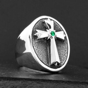 Silver ring with a cross and green gem on a black background.