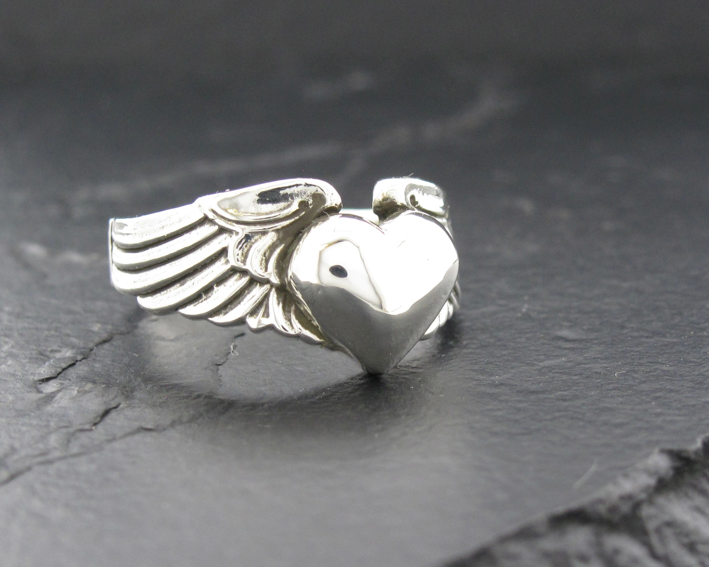 Silver heart-shaped ring with wings on a dark surface.