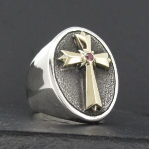 Silver ring with a cross and red gemstone centerpiece.