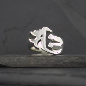 Silver ring with a gothic letter design on a dark surface.