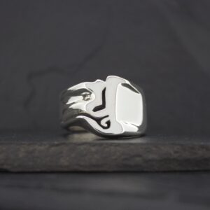 A silver ring with a flame design on a dark surface.