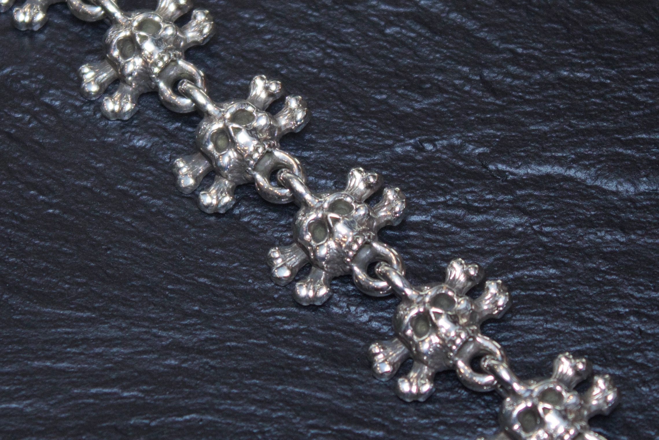 Close-up of a silver floral chain bracelet on a dark surface.