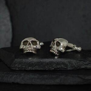 Silver skull cufflinks on a dark surface.