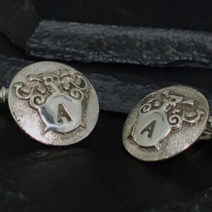 Close-up of silver cufflinks with engraved 'A' initials and ornate designs.