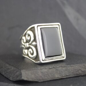 Silver ring with a rectangular black stone and ornate side details.
