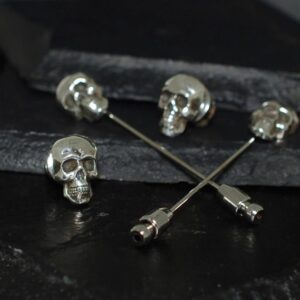 Silver skull-themed pins on a dark surface.